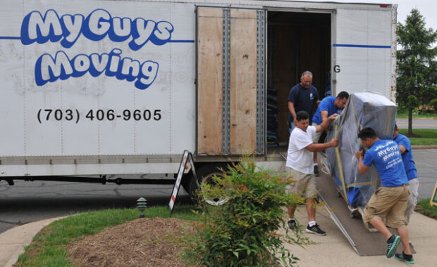 mg moving teams carrying a packed piano down a ramp