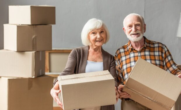 senior couple holding cardboard boxes and looking at camera in new house, moving concept