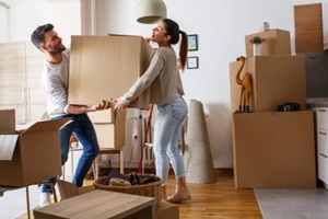 young married couple carrying big cardboard box into new home