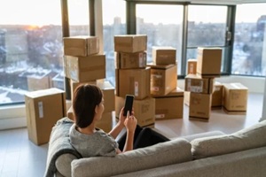 home move out of apartment moving boxes woman using online movers services on mobile phone app easy pick-up with packages for new home